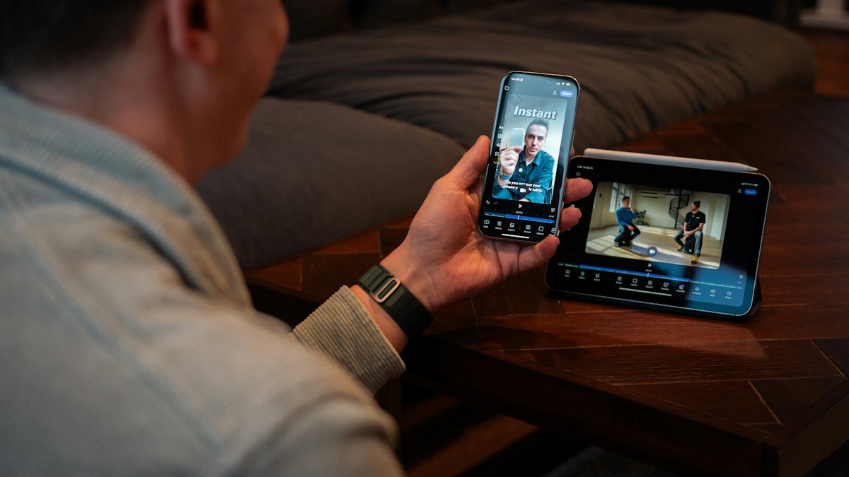 A man holding a phone watching a video next to a monitor
