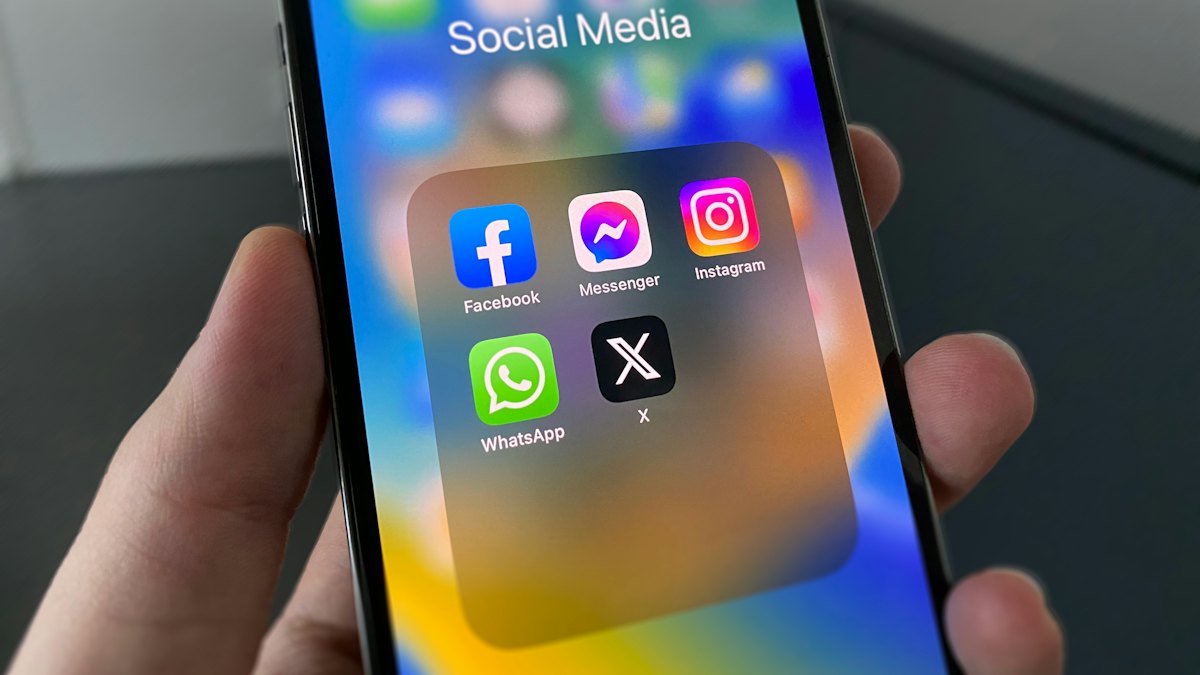 An iPhone in a hand showing a folder of social media apps