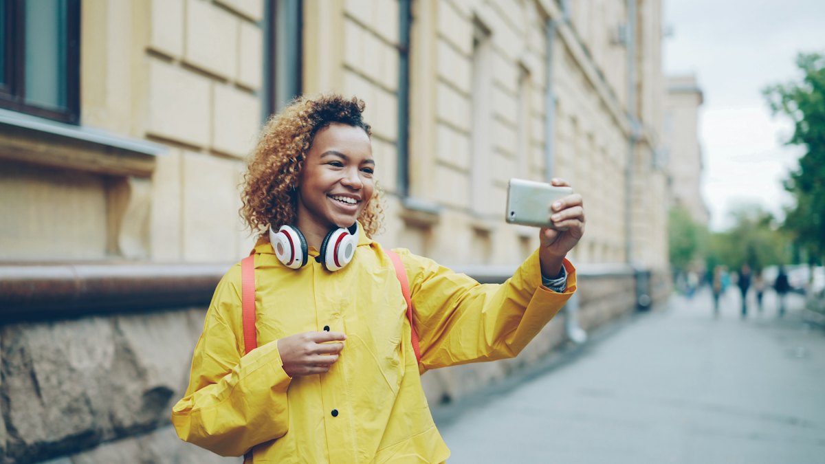 A smiling woman recording herself with her phone on a city street