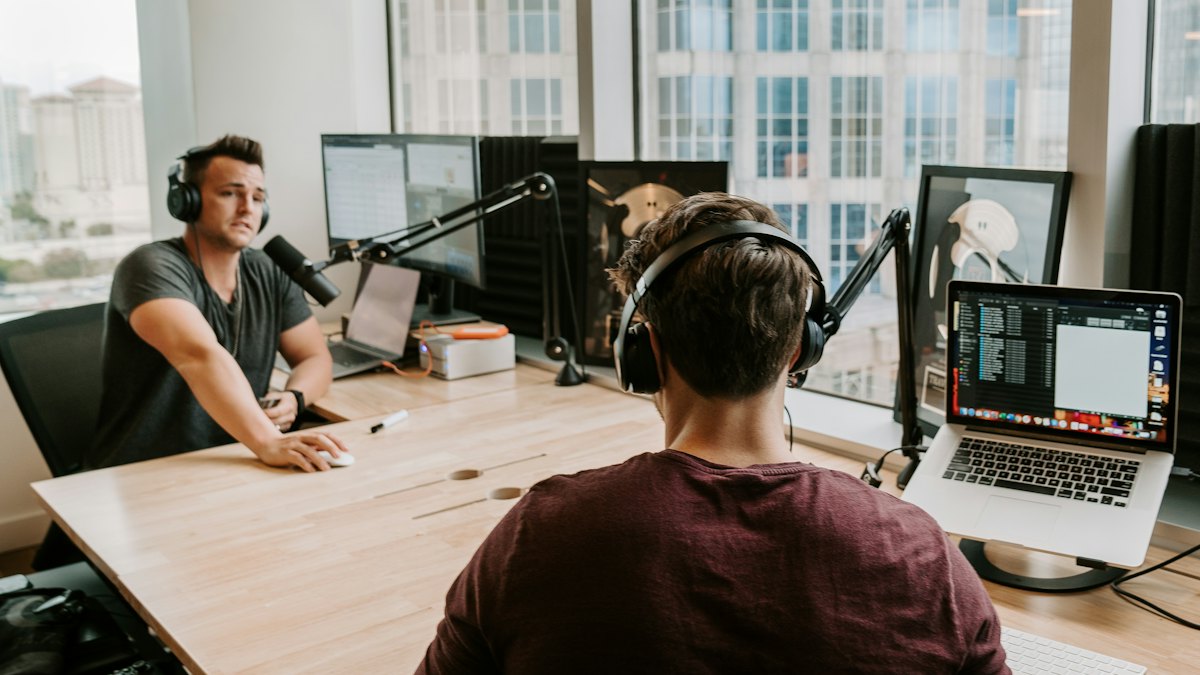 Two people recording a podcast with microphones and headphones in a studio