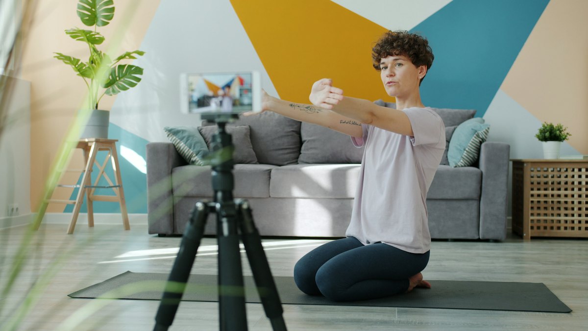 A woman recording a yoga video with a phone on a tripod